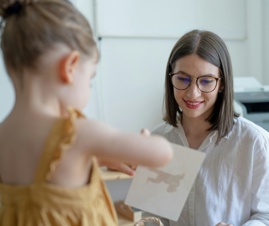 A young girl is showing her drawing to a young female teacher. The teacher is smiling. Photo by Sebastian Pandelache on Unsplash